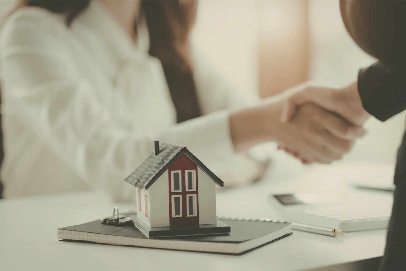 A handshake over a desk with a small model house